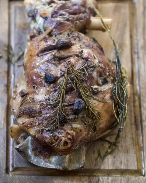 Slow roast shoulder of lamb with garlic and rosemary, on wooden carving board