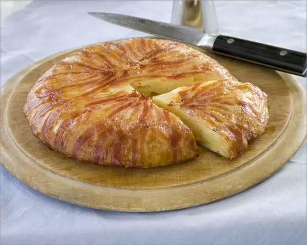 Potato galette wrapped in bacon on wooden board with knife credit: Marie-Louise
