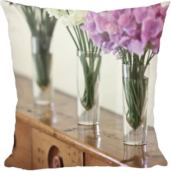 Three simple bunches of different coloured sweet peas in tall glasses on old wooden