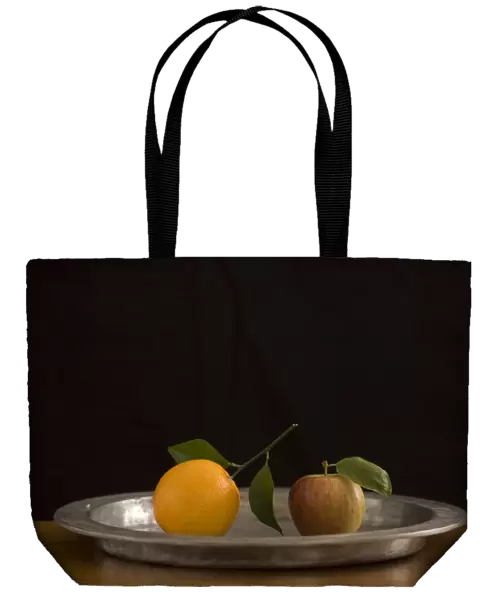 Apple and orange with leaves on pewter charger with black background credit: Marie-Louise