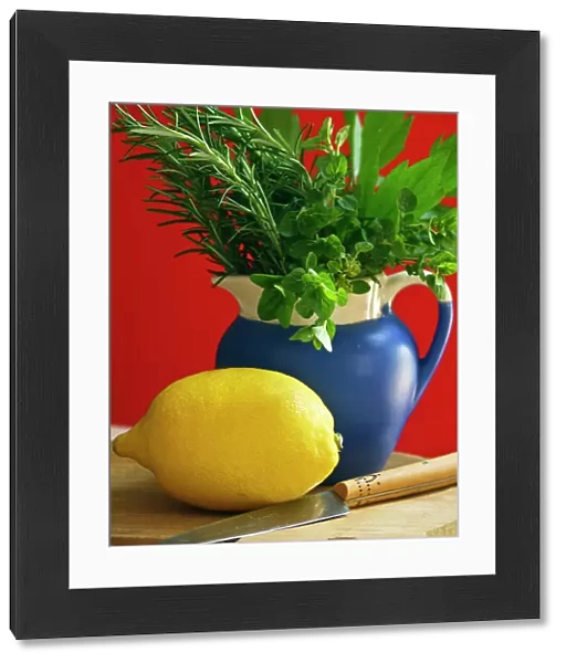 Lemon on chopping board with knife and bunch of mixed garden herbs in blue jug against