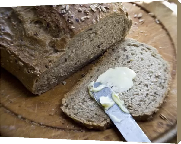 Buttering a slice of bread from a wholegrain, rye and walnut loaf on old wooden board