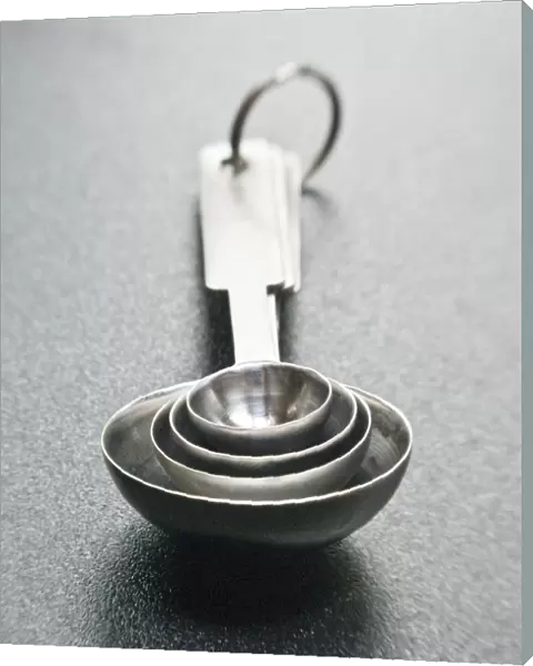 Stainless steel set of measuring spoons, on dark surface. credit: Marie-Louise