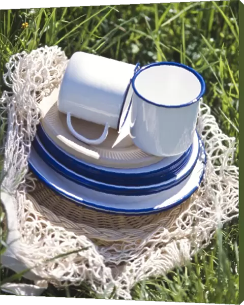 Enamel and paper cups and saucers piled up on a string bag on the grass - part of
