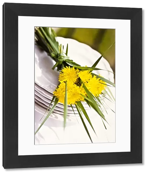 Bouquet of dandelions and long blades of grass on stack of white plates as table