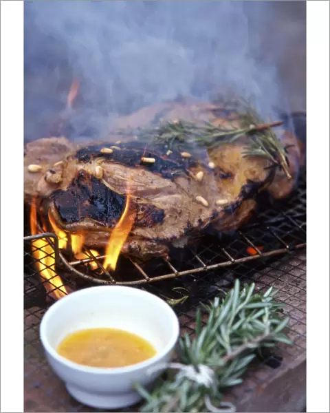Leg of lamb, butterflied to flatten being barbecued on charcoal grill with rosemary