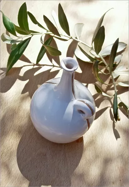 Ceramic oil bottle on tabled dappled in Italian sunshine with branch from olive tree