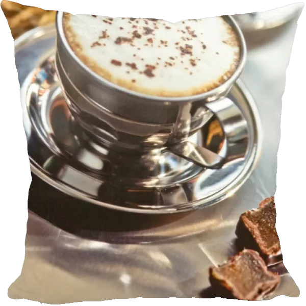 Stainless steel cup of cappucino on metal counter with chocolate fudge and pthysalis