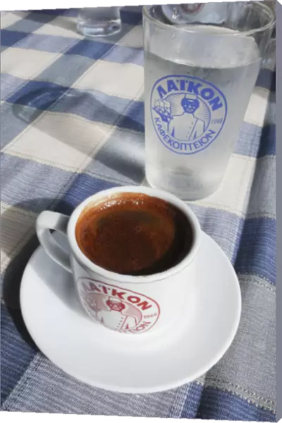 Little cup of strong Greek coffee, with glass of water on table of beach restaurant