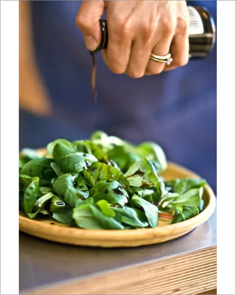 Drizzling balsamic vinegar onto lambs lettuce in pottery dish. credit: Marie-Louise