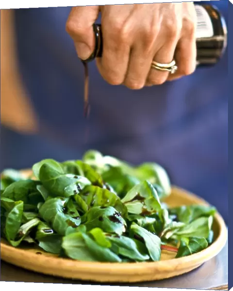 Drizzling balsamic vinegar onto lambs lettuce in pottery dish. credit: Marie-Louise