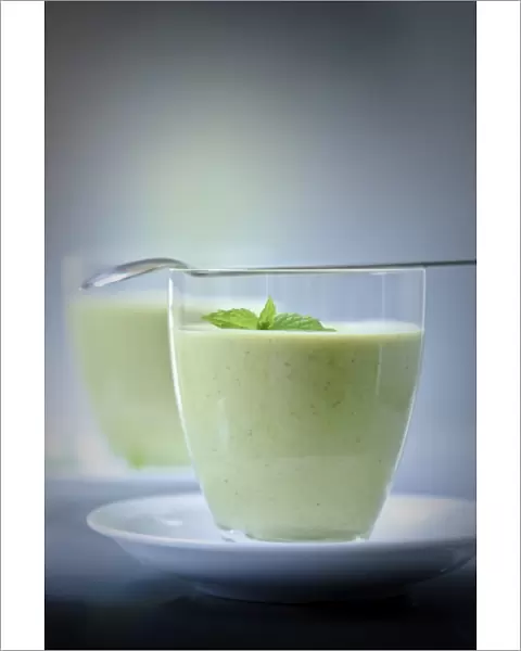 Chilled soup of fresh garden peas and courgettes in small glasses on white saucers