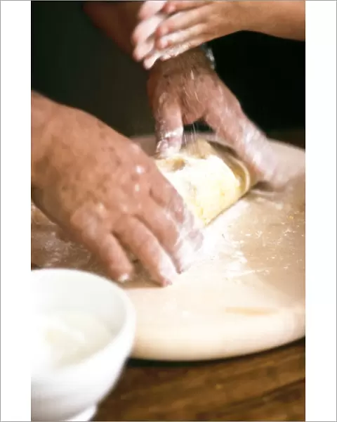 Chef kneading and rolling pastry with little girl helping - hands only shown credit