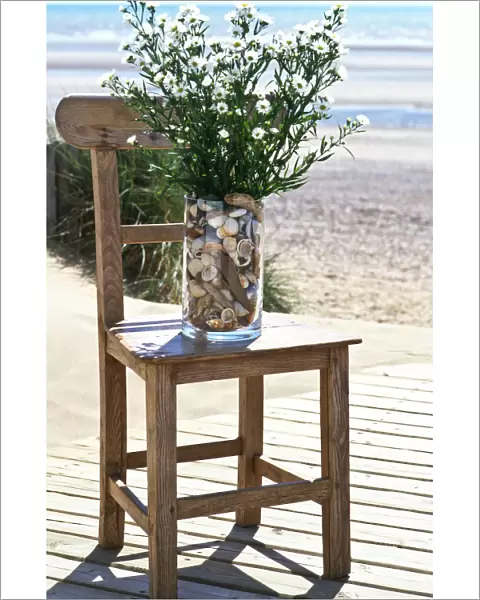 Bunch of michaelmas daisies in pebble filled vase on old chair on decking by the
