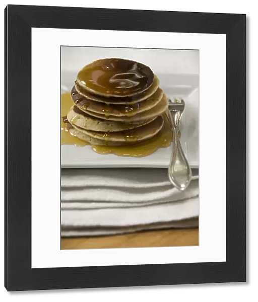 Stack of Scotch pancakes on white plate with silver fork and maple syrup credit