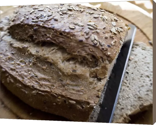 Slicing a wholegrain, rye and walnut loaf on old wooden board. credit: Marie-Louise