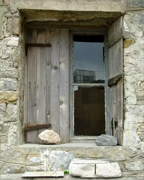 Deep set window in stone building with old weathered shutters held in place with a rock