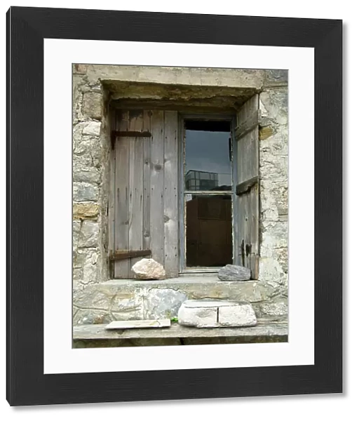 Deep set window in stone building with old weathered shutters held in place with a rock
