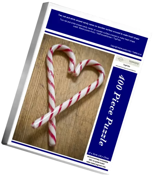 Two red and white striped candy canes on wooden surface crossed to make heart shape