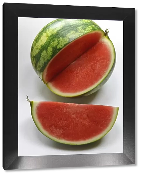 Small watermelon on white surface with quarter cut out showing red flesh credit