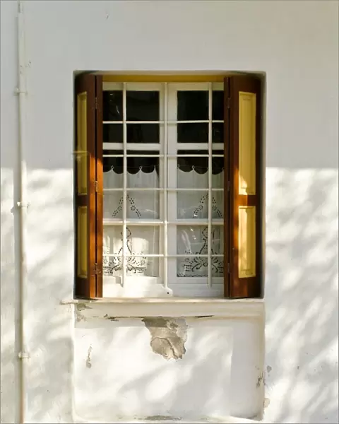 Window in white house in dappled sunlight with white embroidered cutwork curtain
