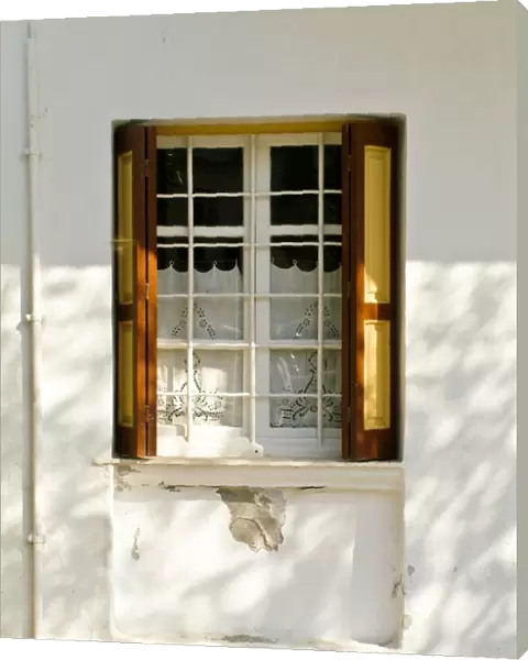 Window in white house in dappled sunlight with white embroidered cutwork curtain