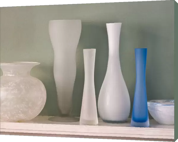 A collection of ground glass vases on mantel shelf, against, green wall credit