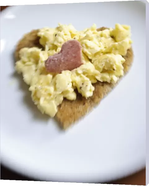 Valentines day breakfast of scrambled eggs on heart shaped toast with slice of salami