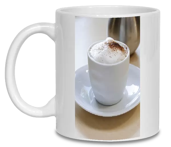 Frothy topped cappuccino in handleless cup with cocoa dusted on and cocoa shaker