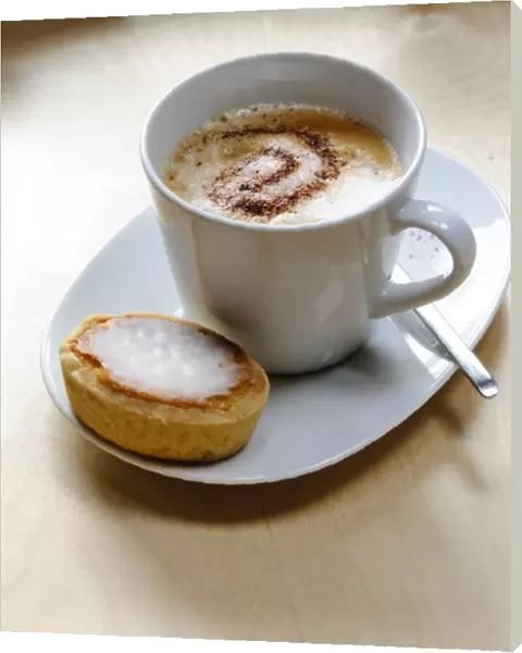 Cup of cappuccino with spiral of cocoa dusted on top with Swedish almond tart credit