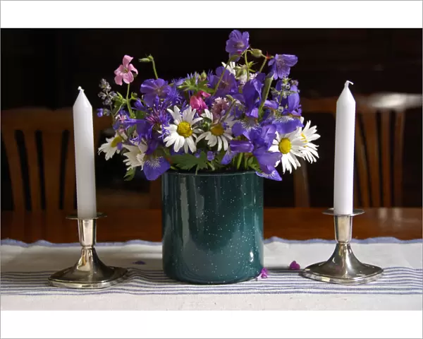 Bouquet of country garden flowers in enamel pot on table with silver candlesticks