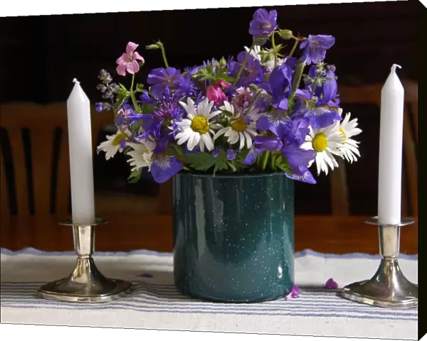 Bouquet of country garden flowers in enamel pot on table with silver candlesticks