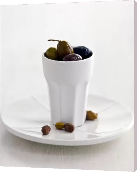 Mixed Italian olives in tall white ceramic pot on white plate with stones on white