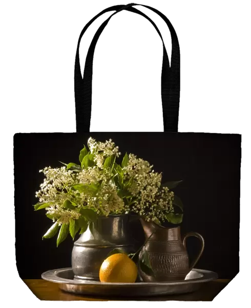 Elderflowers and orange with leaves on pewter charger with black background credit