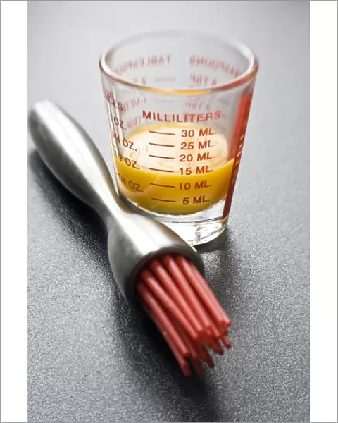 Egg yolk in small glass measuring glass with modern pastry brush with red silicone