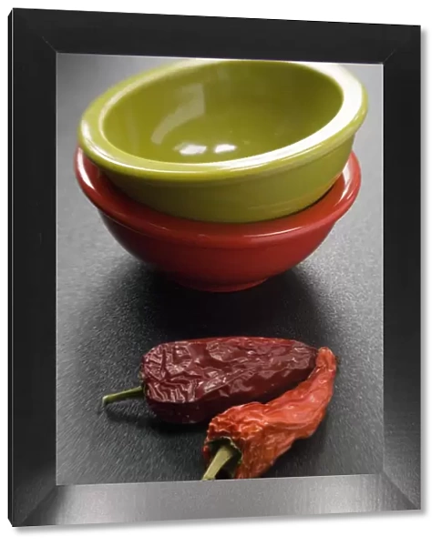 Two bright melamine bowls stacked on dark surface with two red hot chilli peppers