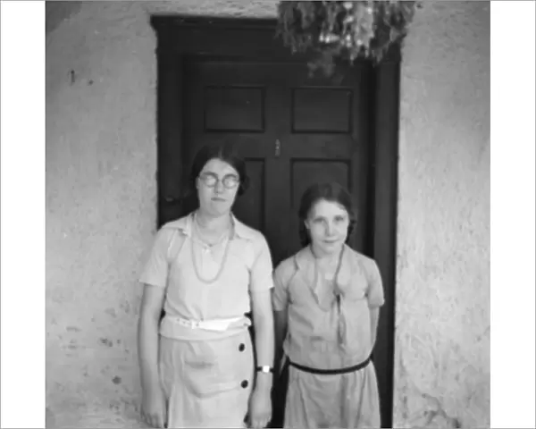 Two sisters pose in front of a cottage. 1936