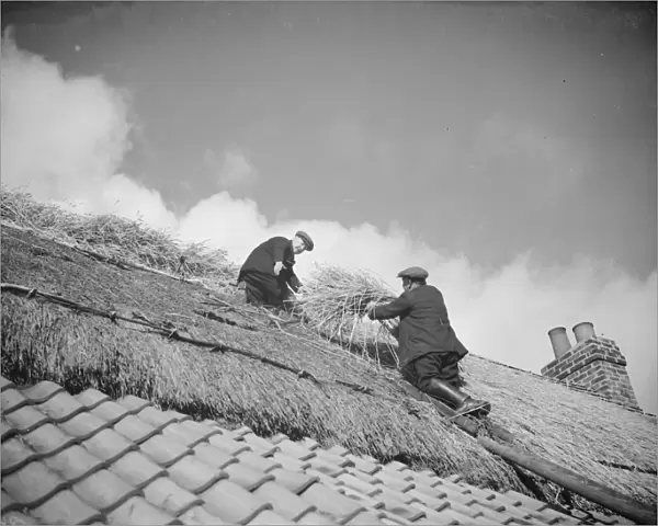 Men work on a tiled roof putting thatching on the roof of a cottage in Orpington