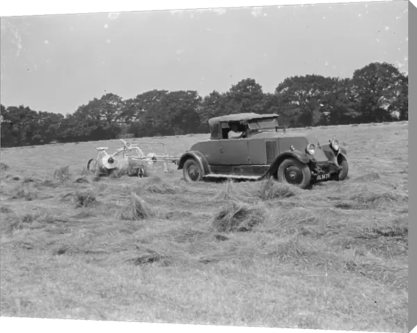 A farmer haymaking in a field using a car to pull the machinery. 1939
