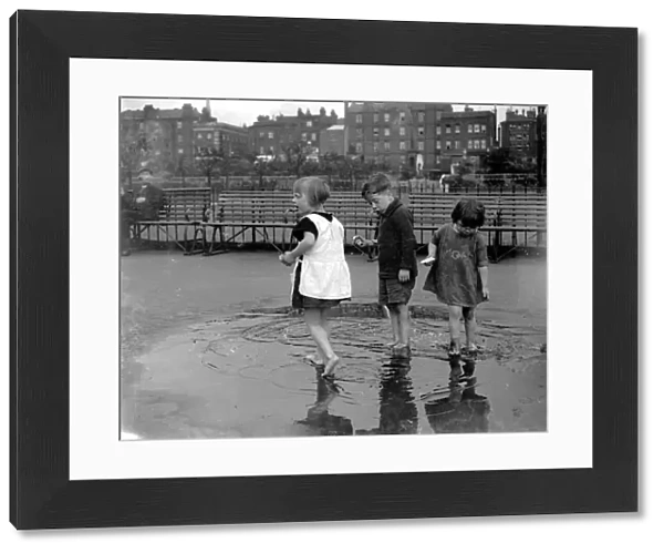 Small children paddling in a puddle in Wapping, London. 1933