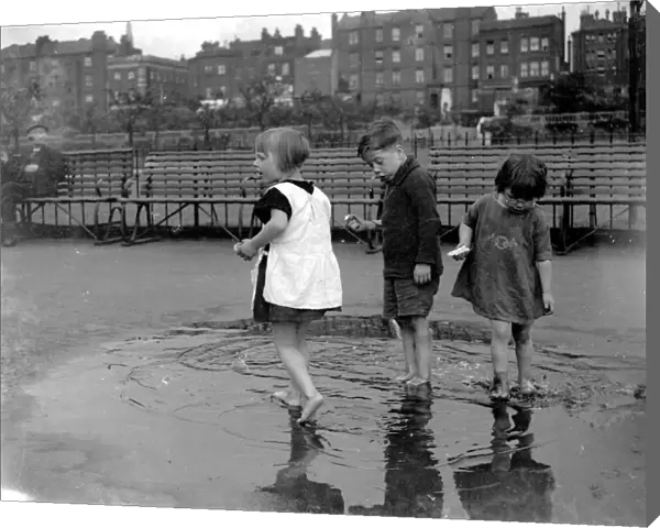 Small children paddling in a puddle in Wapping, London. 1933