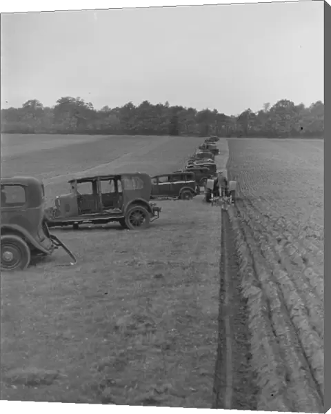 A farmer ploughing a field with a tractor. Alongside are old cars which have been