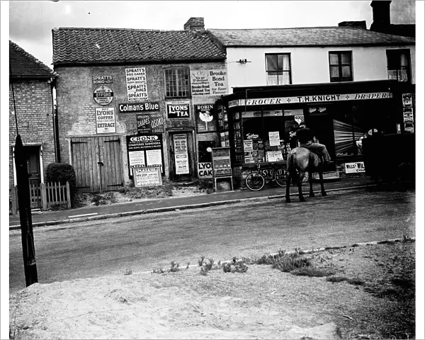 Man on horseback in front of grocers shop around Sevenoaks area, Kent. Advertisements and signs