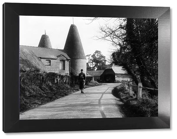 A man walks down a country road passing an oast house, near Penshurst, Kent, England