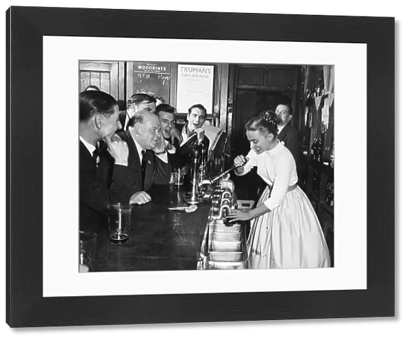A woman barmaid pulls a pint of beer for male customers in a London pub, England. 1950s