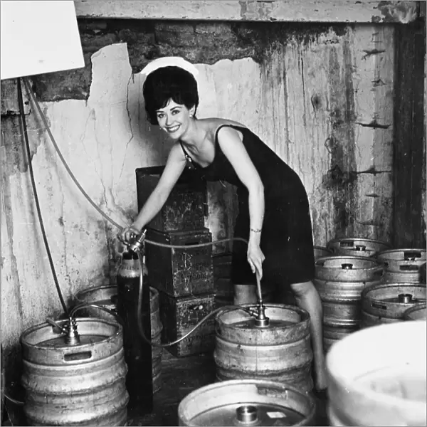 Glamour in the cellar as barmaid Lois taps another barrel of beer. 19 October 1963