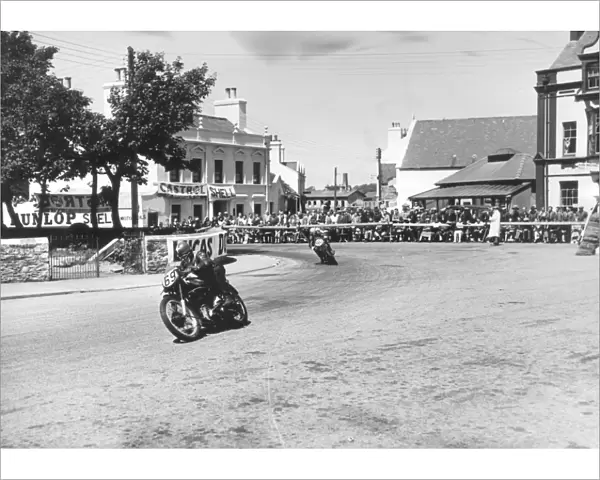 Competitors passing Ramsay Town Square at speed. Number 69 is W. J. Evans on AJS and number 90 is C