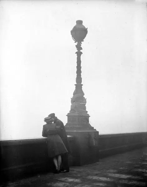 Couple arm in arm leaning over bridge in London in fog 1940s love couple romance