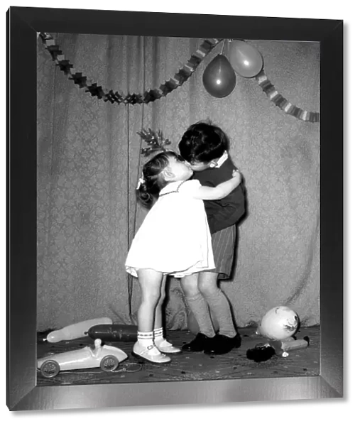 A little boy and girl kissing under the mistletoe at a Christmas party