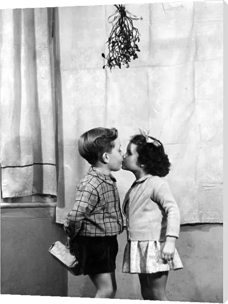 Young boy and girl kissing underneath the mistletoe at Christmas time 1956 love